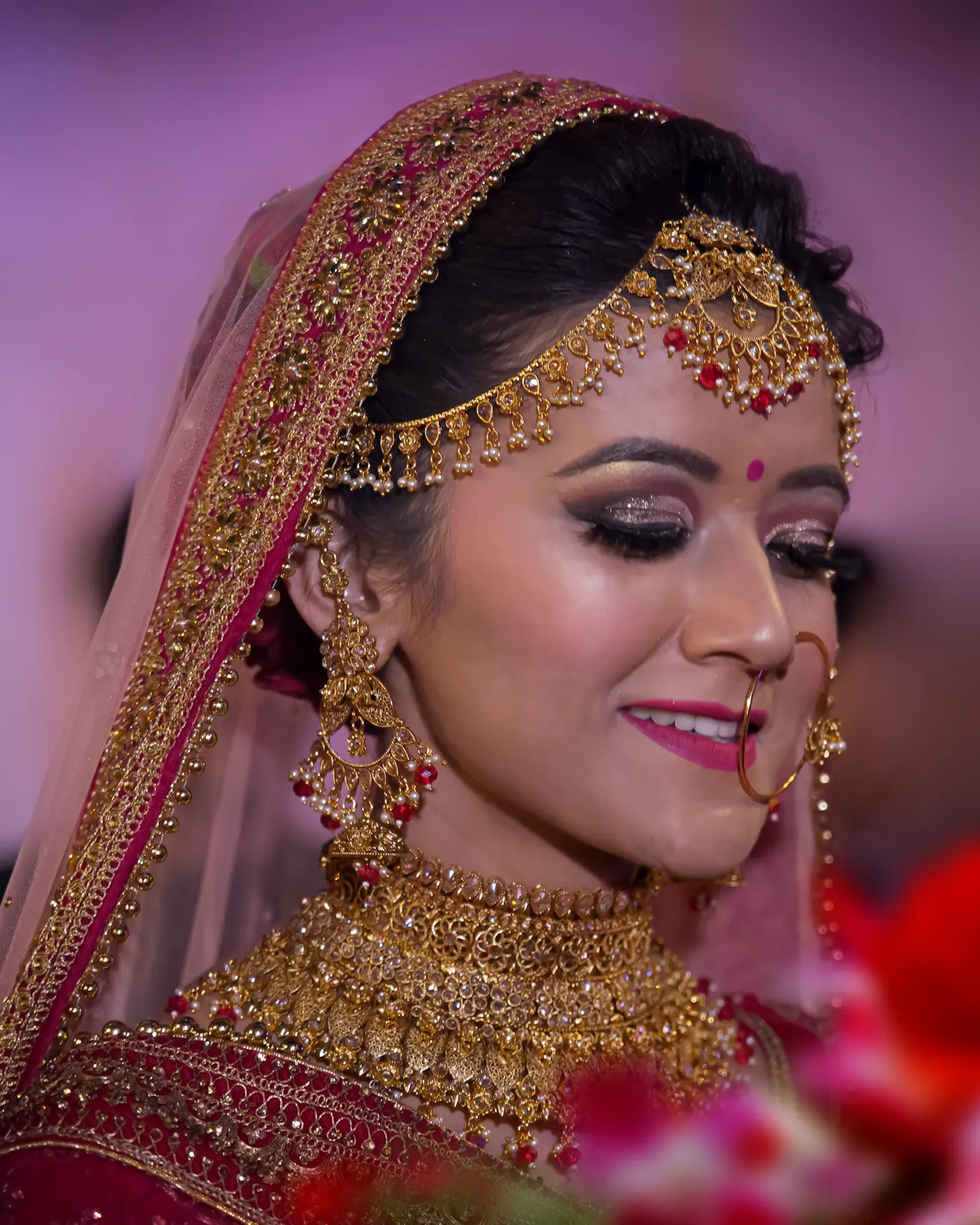 Close-up of an Indian bride in a red dupatta with gold maang tikka, nose ring and bridal makeup