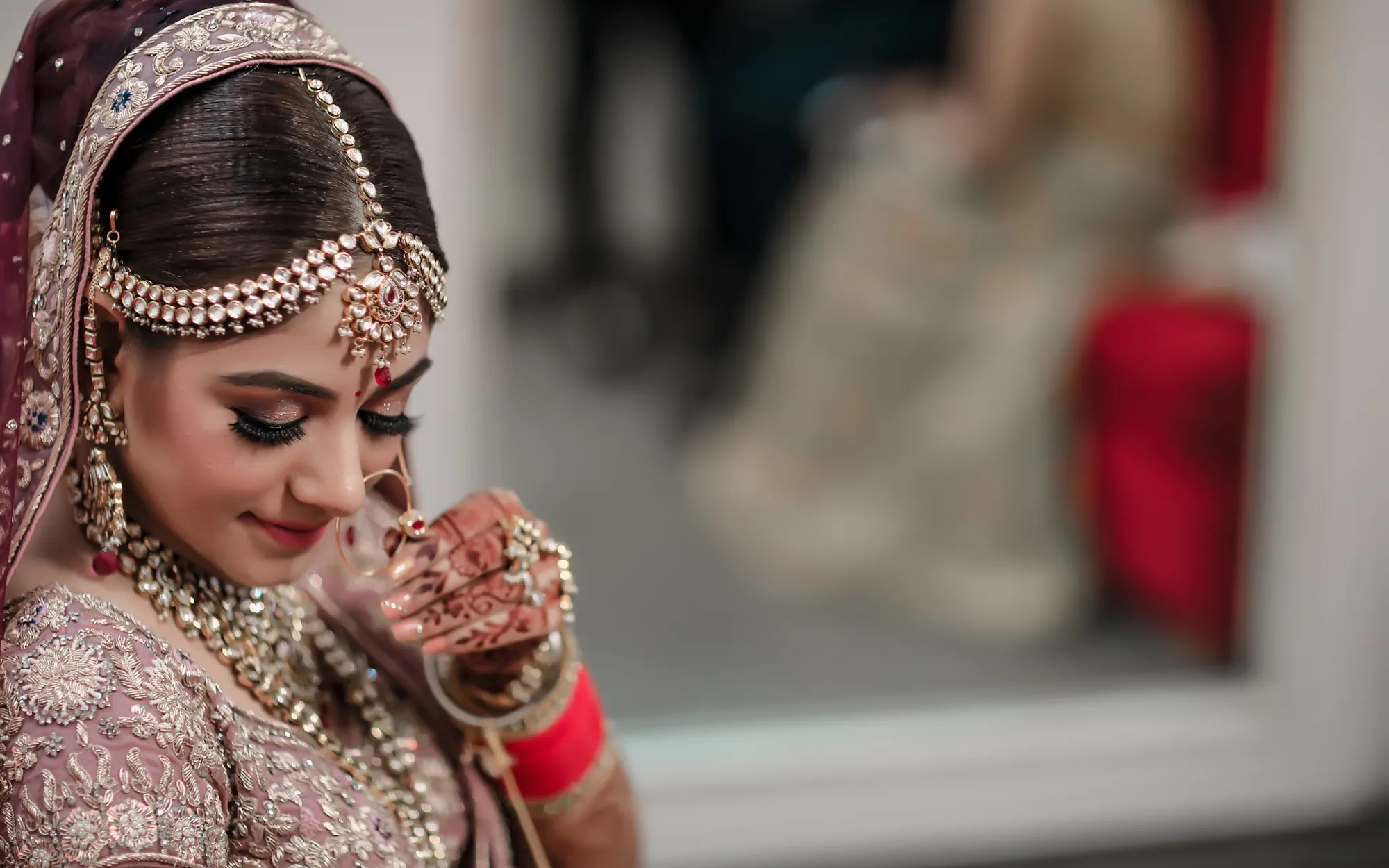 Indian bride in a blush pink lehenga with kundan maang tikka, nath and mehndi, smiling softly in HD bridal makeup